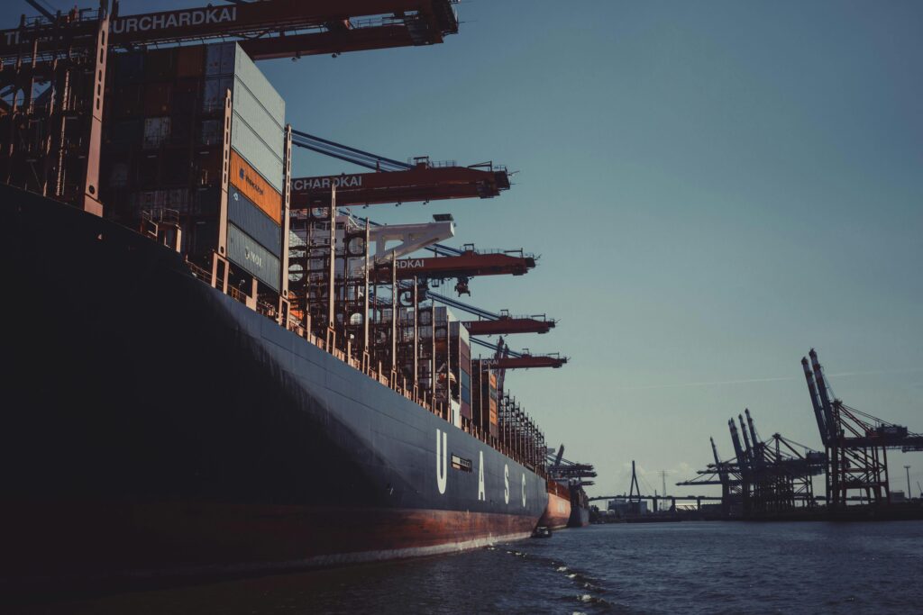 A large cargo ship docked at Hamburg Harbor, cranes loading containers under a clear sky.