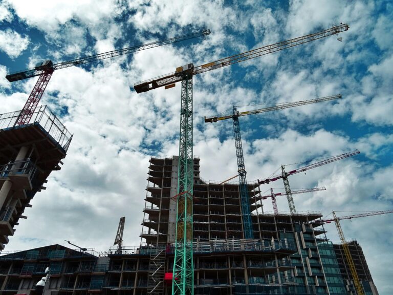 Urban construction site with numerous cranes framing rising skyscrapers against a blue sky.